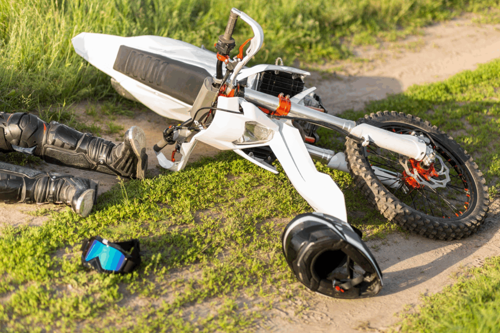 Downed motorcycle and safety gear on a dirt path, illustrating the aftermath of an off-road or motorcycle accident.